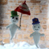 Deux versions de Gaspard le fantôme blanc au crochet. L'un portant un chapeau vert, Il tient un parapluie rouge et crème dans sa main. L'autre portant un chapeau violet décoré de fleurs en perles. Ils se tiennent devant un mur en pierre avec une sorte de nuage blanc en bas.