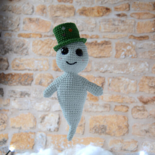Gaspard le fantôme blanc au crochet portant un chapeau vert. Il se tient devant un mur en pierre.