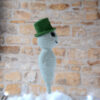 Gaspard le fantôme blanc au crochet, tourné vers le côté droit. Il porte un chapeau vert et se tient devant un mur en pierre.