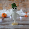 Gaspard le fantôme blanc au crochet, sur un socle en bois. Il porte un chapeau vert et se tient devant un mur en pierre. On distingue en fond flouté, un nuage blanc ainsi qu'une guirlande lumineuse, avec des citrouilles et une oie citrouille posées devant.