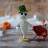 Gaspard le fantôme blanc au crochet, sur un socle en bois. Il porte un chapeau vert et a un parapluie posé à côté de lui. Il se tient devant un mur en pierre. On distingue en fond flouté, un nuage blanc ainsi qu'une guirlande lumineuse, avec des citrouilles et une oie citrouille posées devant.