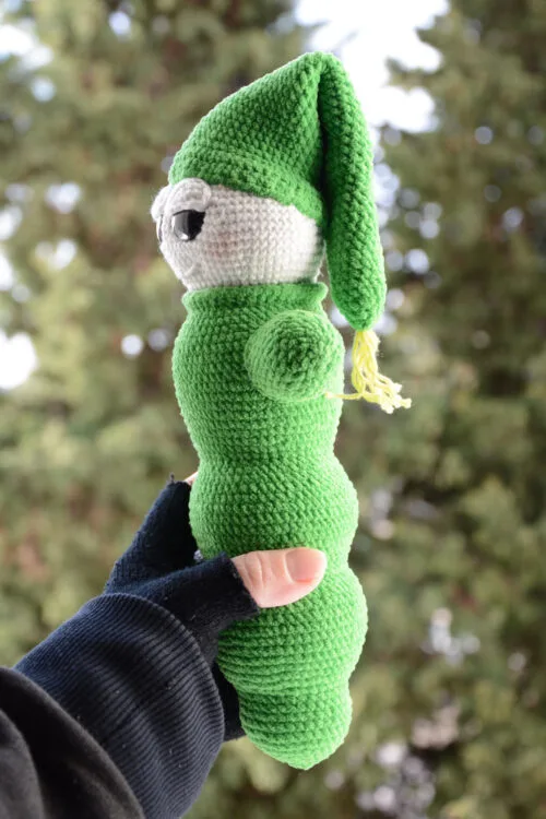 Luciole au crochet vue de profil, montrant sa forme allongée et son bonnet pointu vert, tenue dans une main, avec un arrière-plan naturel flou.