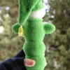 Luciole au crochet vue de dos, montrant sa forme allongée et son bonnet pointu vert, tenu dans une main, avec un arrière-plan naturel flou.