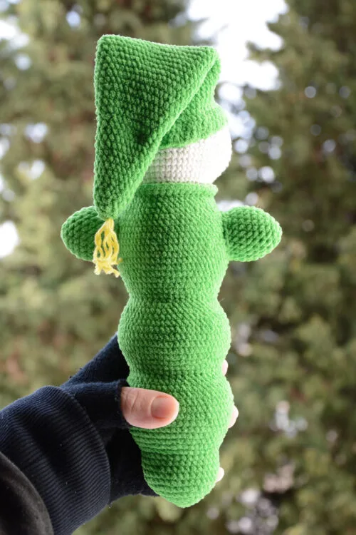 Luciole au crochet vue de dos, montrant sa forme allongée et son bonnet pointu vert, tenu dans une main, avec un arrière-plan naturel flou.