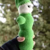 Luciole au crochet vue de son autre profil, montrant sa forme allongée et son bonnet pointu vert, tenue dans une main, avec un arrière-plan naturel flou.