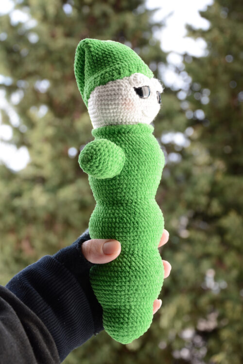 Luciole au crochet vue de son autre profil, montrant sa forme allongée et son bonnet pointu vert, tenue dans une main, avec un arrière-plan naturel flou.