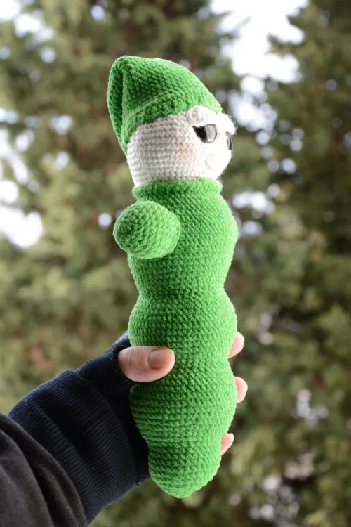Luciole au crochet vue de son autre profil, montrant sa forme allongée et son bonnet pointu vert, tenue dans une main, avec un arrière-plan naturel flou.