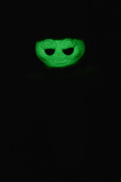 Luciole au crochet photographiée dans l'obscurité, faisant ressortir le fil phosphorescent dans le noir et révélant son visage lumineux.