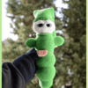 Luciole au crochet, de couleur verte avec un visage clair et de grands yeux. Elle porte un bonnet et est tenue dans une main, photographiée en extérieur devant un arrière-plan naturel flou.