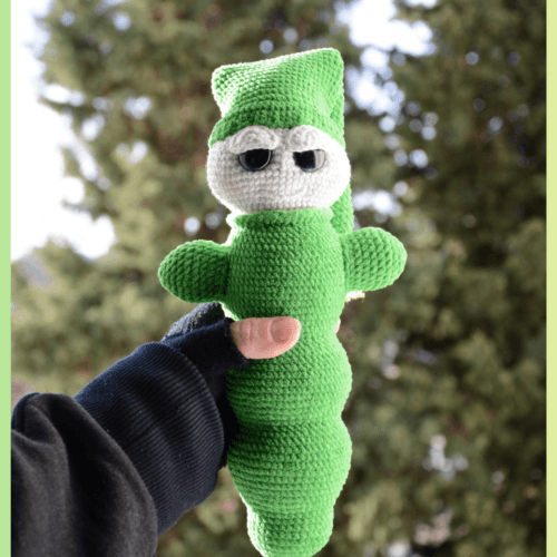 Luciole au crochet, de couleur verte avec un visage clair et de grands yeux. Elle porte un bonnet et est tenue dans une main, photographiée en extérieur devant un arrière-plan naturel flou.