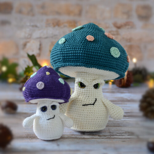 Deux amigurumis champignons Ottie, un grand bleu pétrole et un petit violet, posés côte à côte sur un décor en bois.