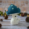 Champignon au crochet, avec un chapeau bleu pétrole décoré de spots rose et vert d'eau. Il est photographié tourné vers le côté droit.