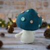 Champignon au crochet, avec un chapeau bleu pétrole décoré de spots rose et vert d'eau. Il est photographié tourné de dos.