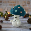 Champignon au crochet, avec un chapeau bleu pétrole décoré de spots rose et vert d'eau. Il est photographié tourné vers le côté gauche.