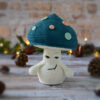 Champignon au crochet, avec un chapeau bleu pétrole décoré de spots rose et vert d'eau. Il est photographié de face, et ses paupières lui donne un airsongeur et lointain.