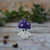 Petit champignon au crochet, avec un chapeau violet décoré de spots colorés. Il est photographié de face, sans paupières.