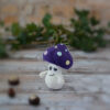 Petit Ottie champignon au crochet, avec un chapeau violet décoré de spots colorés. Il est tourné vers le côté gauche, révélant mieux ainsi ses paupières