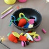 Un bol noir rempli de bonbons crochetés colorés avec notamment deux gros en forme de fraises rouges, un œuf au plat, des réglisses, des bananes et autres. Certains de ces bonbons sont disposés devant le bol. En arrière-plan, on aperçoit des pelotes de coton rose et jaune, des crochets ainsi qu'une guirlande lumineuse.