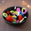 Un bol noir rempli de bonbons crochetés colorés avec notamment deux gros en forme de fraises rouges, un œuf au plat, des réglisses, des bananes et autres. En arrière-plan, on aperçoit une guirlande lumineuse.