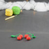 sur un fond gris foncé sont disposés des cerises miniatures crochetés. À l'arrière plan, sur la gauche il y a 2 pelotes jaune et verte et un crochet. En fond est disposé un nuage de ouate et une guirlande lumineuse.