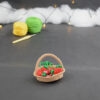 sur un fond gris foncé, il y a un panier crocheté en topaze garni de fruits rouges miniatures : fraises, cerises et baies variées (framboises, mûres,...). À l'arrière plan, sur la gauche il y a 2 pelotes jaune et verte et un crochet. En fond est disposé un nuage de ouate et une guirlande lumineuse.