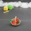 sur un fond gris foncé, il y a un panier crocheté en topaze garni de fruits rouges miniatures : fraises, cerises et baies variées (framboises, mûres,...). À l'arrière plan, sur la gauche il y a 2 pelotes jaune et verte et un crochet. En fond est disposé un nuage de ouate et une guirlande lumineuse.