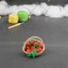 sur un fond gris foncé, il y a un panier crocheté en topaze garni de fruits rouges miniatures : fraises, cerises et baies variées (framboises, mûres,...). À l'arrière plan, sur la gauche il y a 2 pelotes jaune et verte et un crochet. En fond est disposé un nuage de ouate et une guirlande lumineuse.