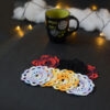 Huit sous-verres ronds crochetés sont posés sur un fond gris sombre. Ils sont de différentes couleurs (dégradé parme et lilas, dégradé orange et jaune, dégradé violet et aubergine et uni noir. En fond il y a une tasse noire à l'intérieur vert clair et des guirlandes lumineuses sont disposées sur du rembourrage blanc façon nuages.