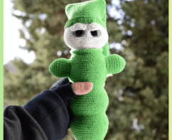 Luciole au crochet, de couleur verte avec un visage clair et de grands yeux. Elle porte un bonnet et est tenue dans une main, photographiée en extérieur devant un arrière-plan naturel flou.
